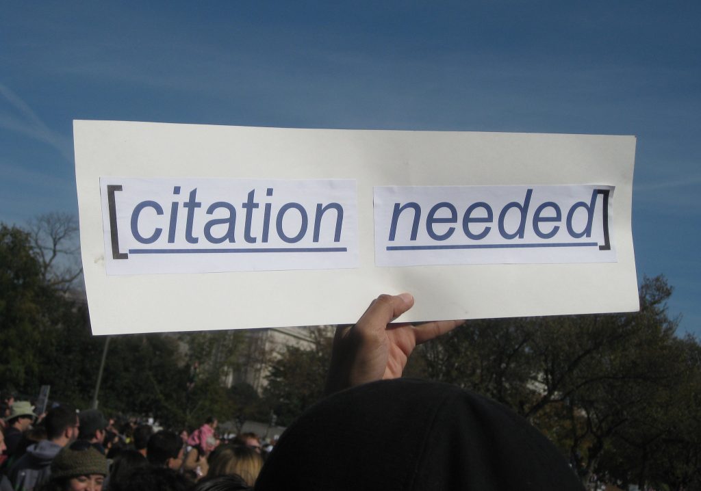Hand holding "citation needed" poster